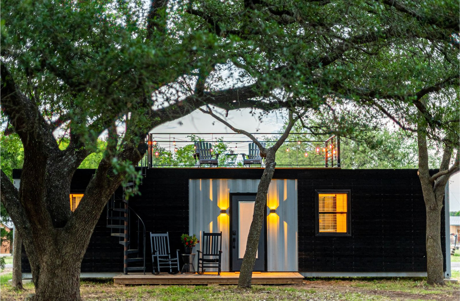 Small tiny home with lights on and tress around it